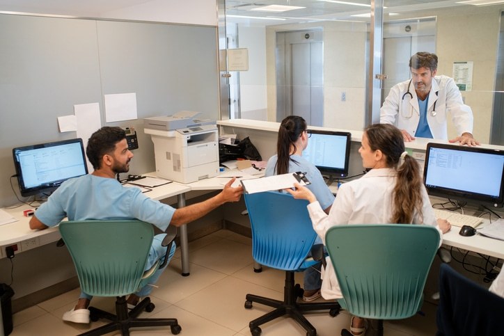 Administrative staff woking at hospital office with doctor standing at front desk